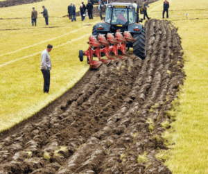 red tractor ploughing a field with onlookers 